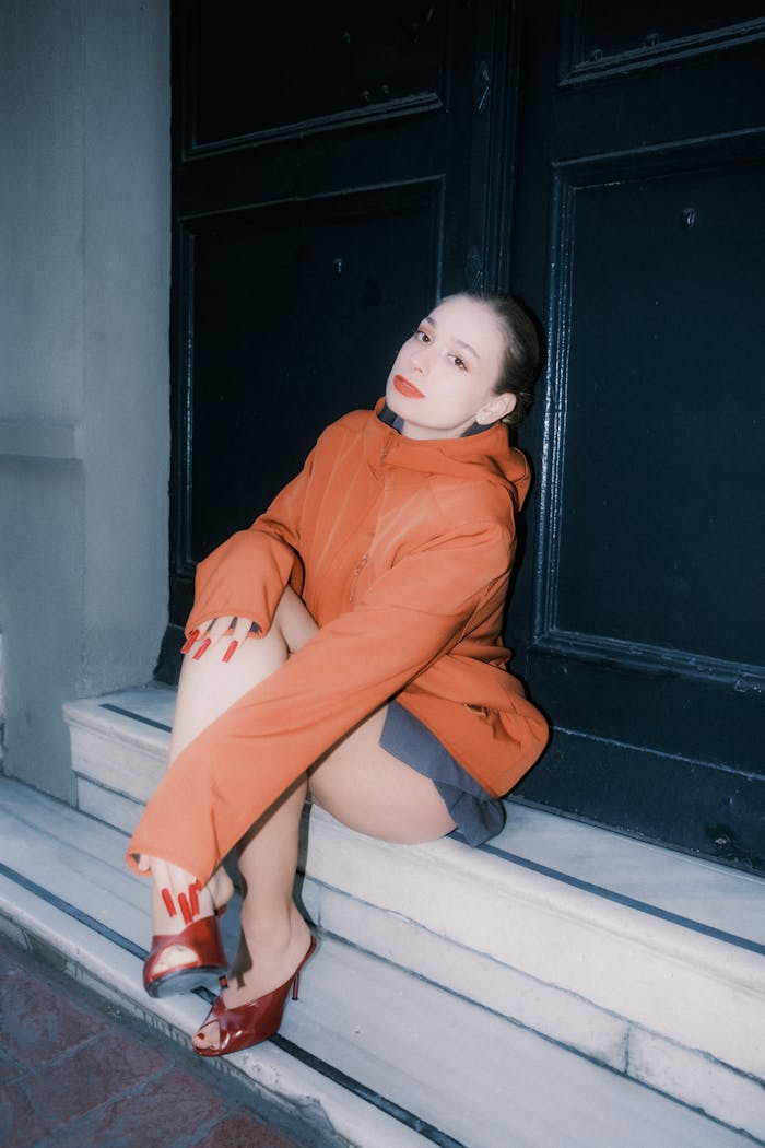 Mastering the First Impression: Your intriguing post title goes here Fashionable woman in orange coat and red shoes sitting on marble steps.